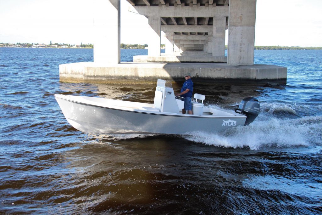 Side view of a whisper grey Atlas Boatworks 23F center console fishing boat running in choppy water under a bridge. 200hp yamaha outboard engine on the back.