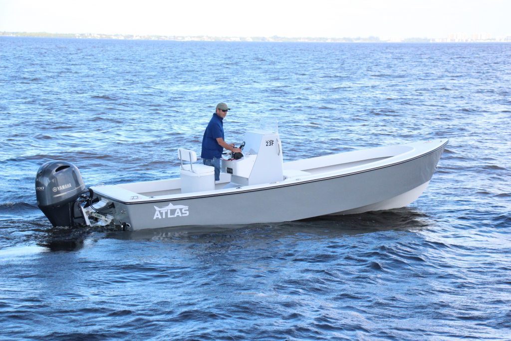 Side view of a whisper grey Atlas Boatworks 23F center console fishing boat idling in choppy water. 200hp yamaha outboard engine on the back.