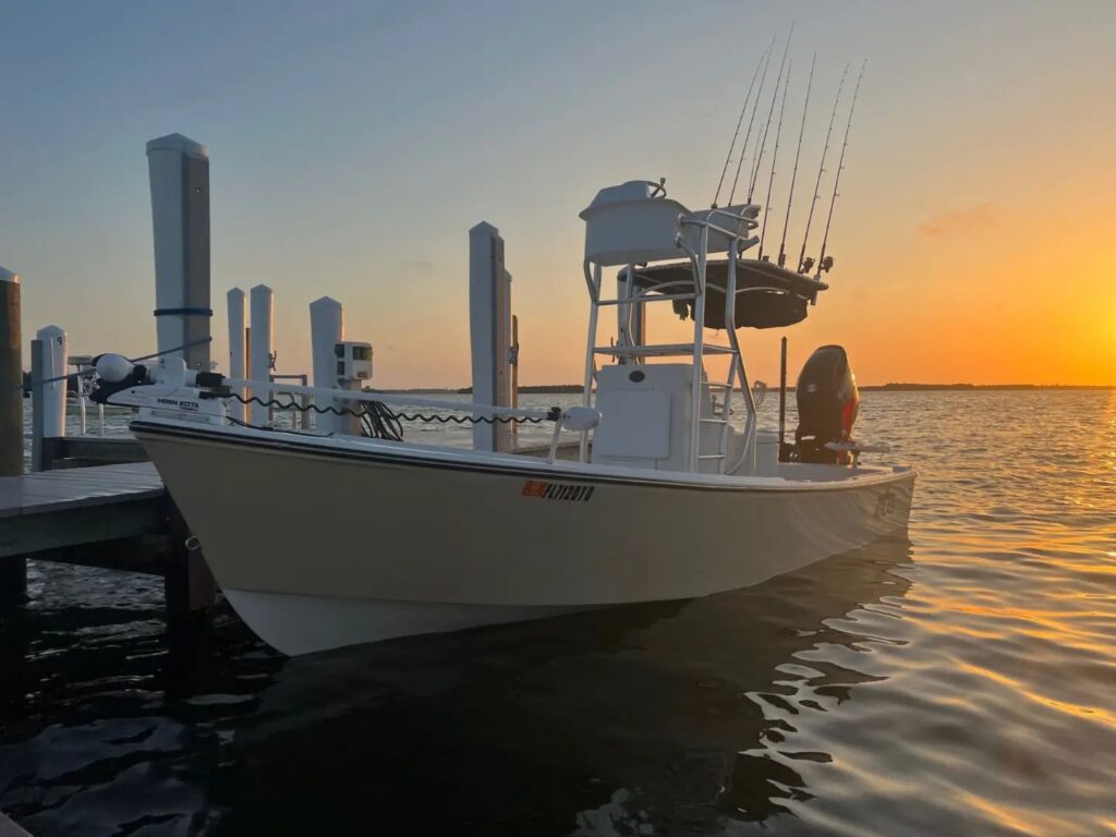 sunset view of tan Atlas Boatworks 23F center console fishing boat tied to a dock. It has a half tower installed with 2nd station up top.