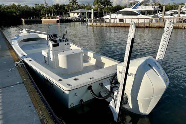 Stern view of ice blue Atlas Boatworks 23F tied to a dock with white porta bracket, white 10-foot blade power pole shallow-water anchors and Mercury 200XS motor.