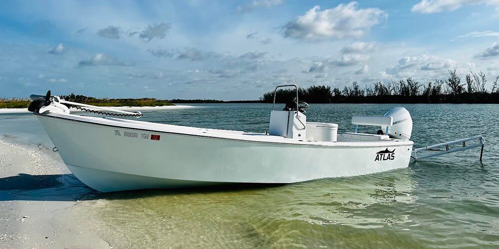Side view of an ice blue Atlas Boatworks 23F center console boat pulled up on the beach and held in place by twin power pole shallow water anchors.