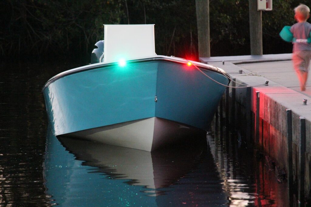 Bow view of boston whaler blue Atlas Boatworks 23F with navigation lights on. Small child running along dock to the right.