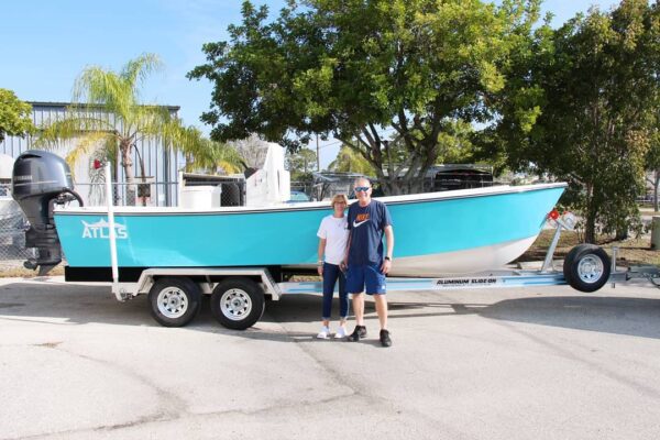 Delivery day of a new boat. A couple stands in front of an boston whaler Atlas Boatworks 23F center console fishing boat on a trailer.