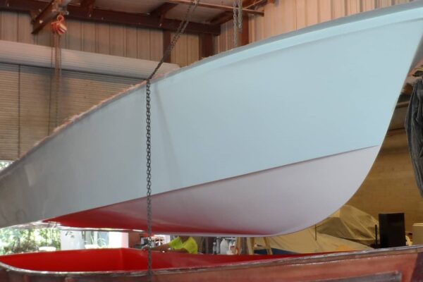 side view of Atlas Boatworks 23F hull being lifted out of a boat mold. Chains from lifting device hang down.