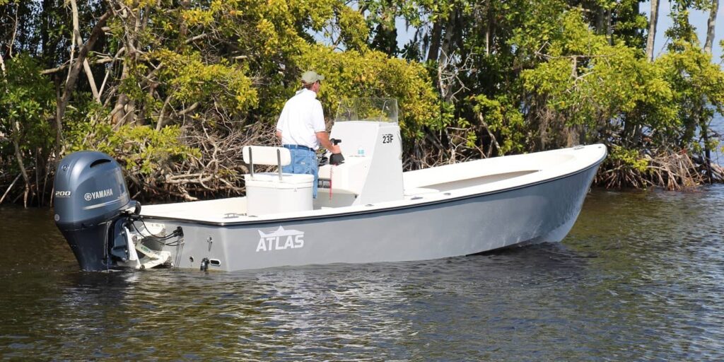 Side view of a whisper grey Atlas Boatworks 23F center console fishing boat idling in calm water. 200hp yamaha outboard engine on the back.