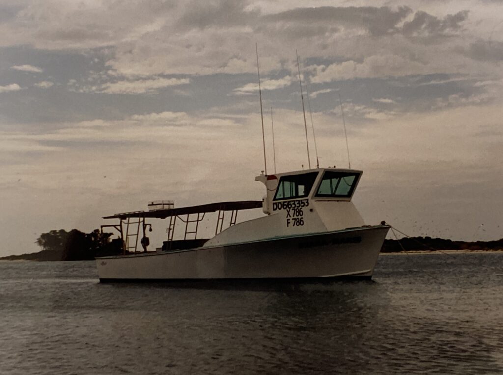 Commercial stone crab and grouper fishing boat name Shana Marie anchored in the harbor of the Dry Tortugas National Park. Fort Jefferson and a lighthouse in the background.