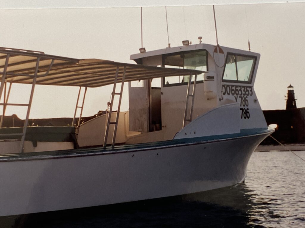 Commercial stone crab and grouper fishing boat name Shana Marie anchored in the harbor of the Dry Tortugas National Park. Fort Jefferson and a lighthouse in the background.