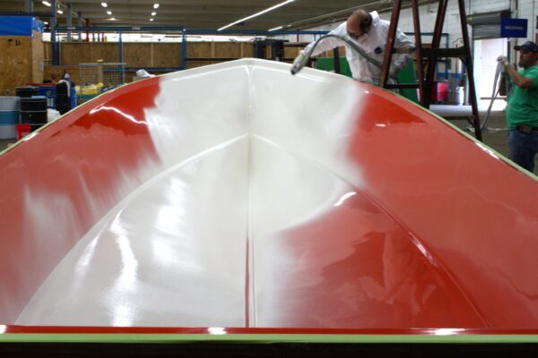 White gelcoat is sprayed into the bow of a red boat mold