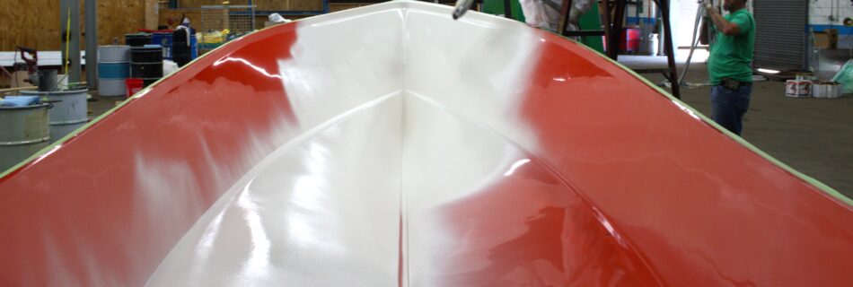 White gelcoat is sprayed into the bow of a red boat mold