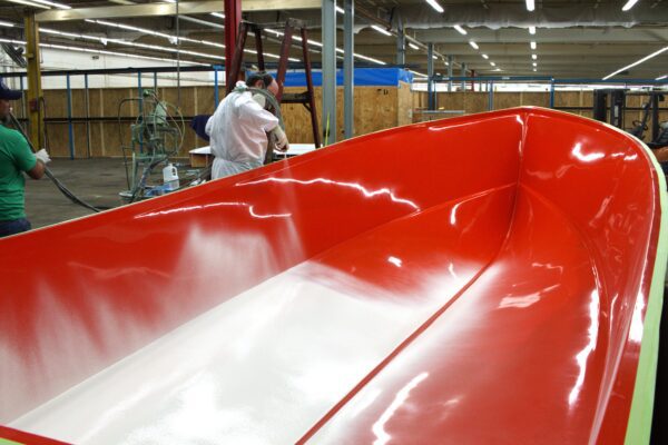 White gelcoat is sprayed into a red boat mold