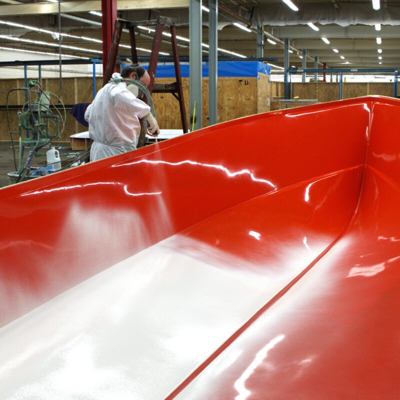 White gelcoat is sprayed into a red boat mold