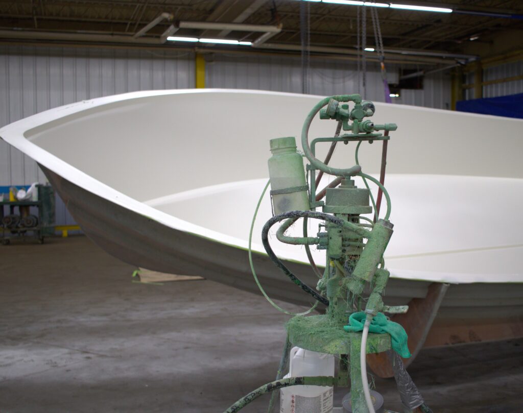 A gelcoat machine sits in front of a boat mold.