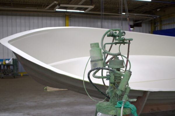 A gelcoat machine sits in front of a boat mold.