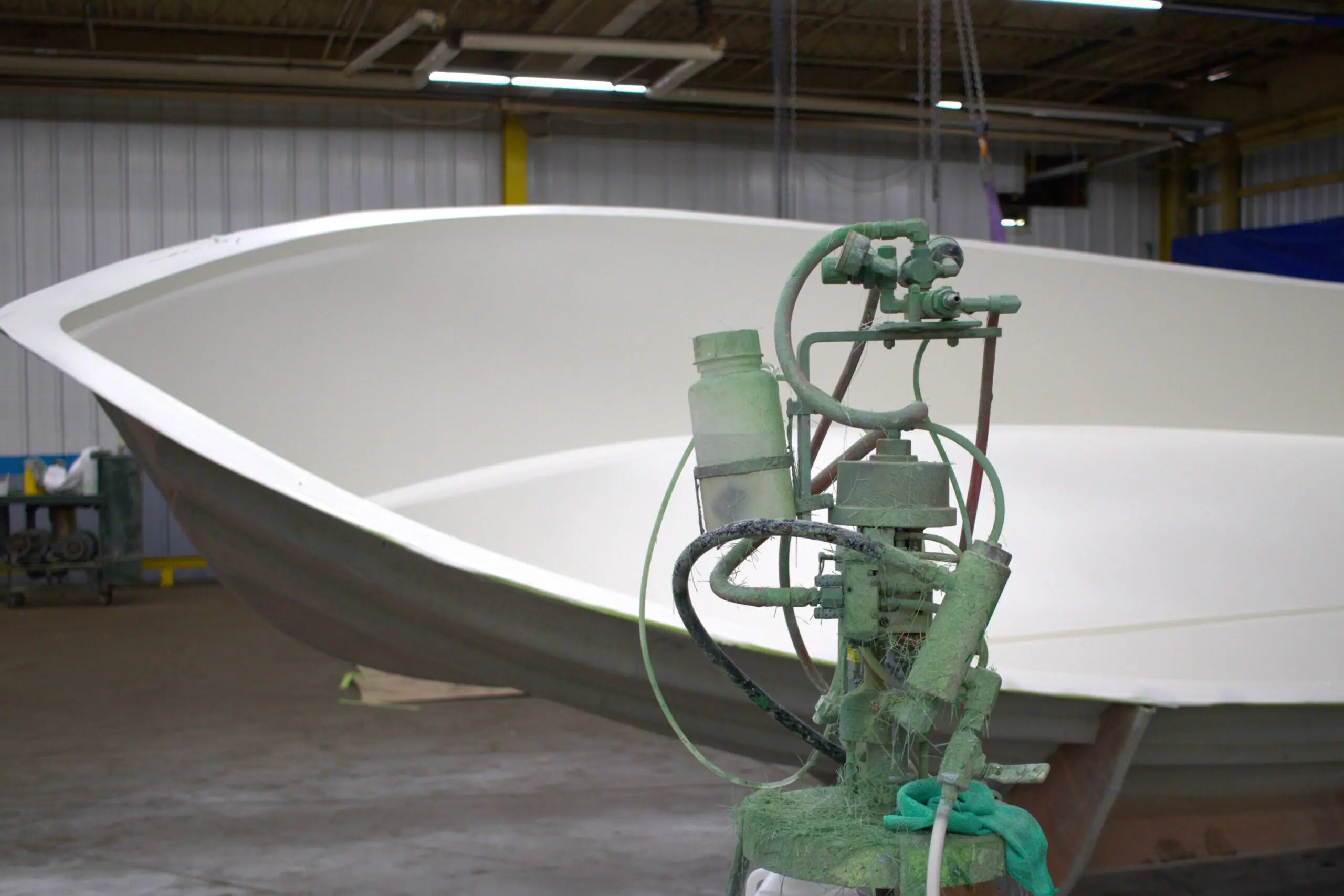 A gelcoat machine sits in front of a boat mold.