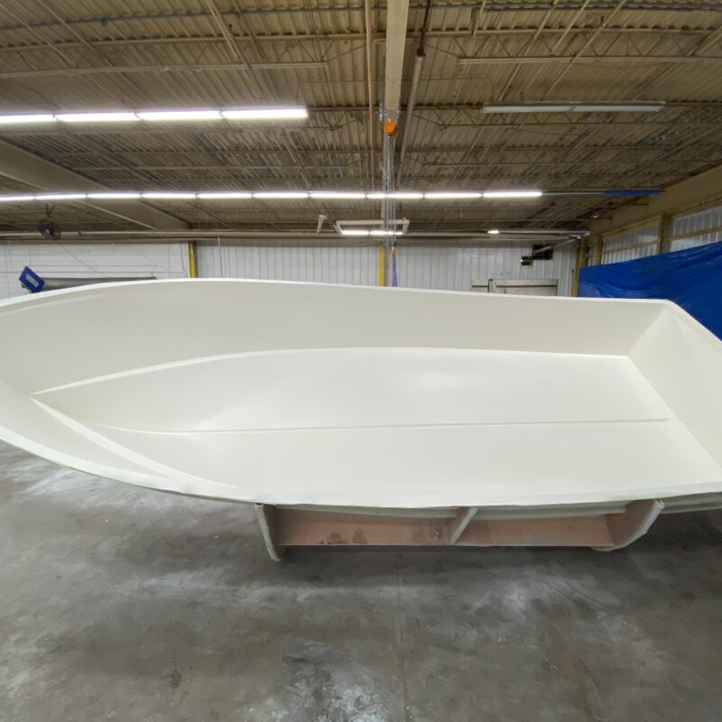 A boat with white gelcoat sits tipped up in the mold