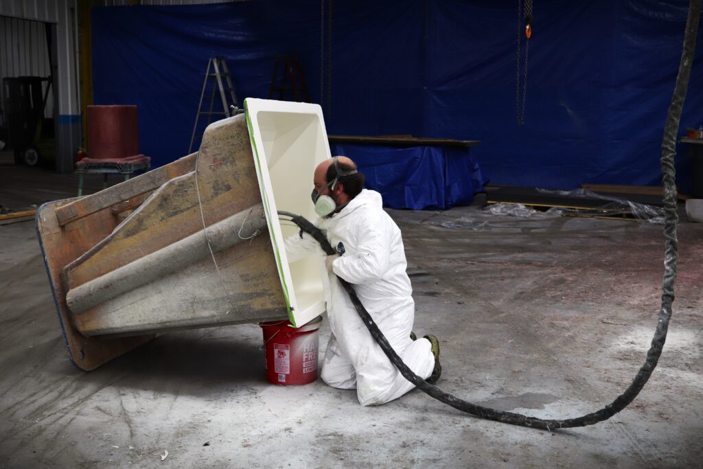 A worker on his knees sprays gelcoat into a center console mold