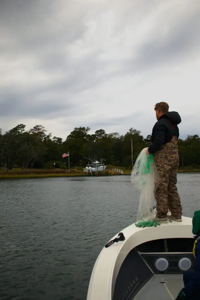 A captain stands on the front deck of the Atlas Boatworks 23F bay bay with a castnet